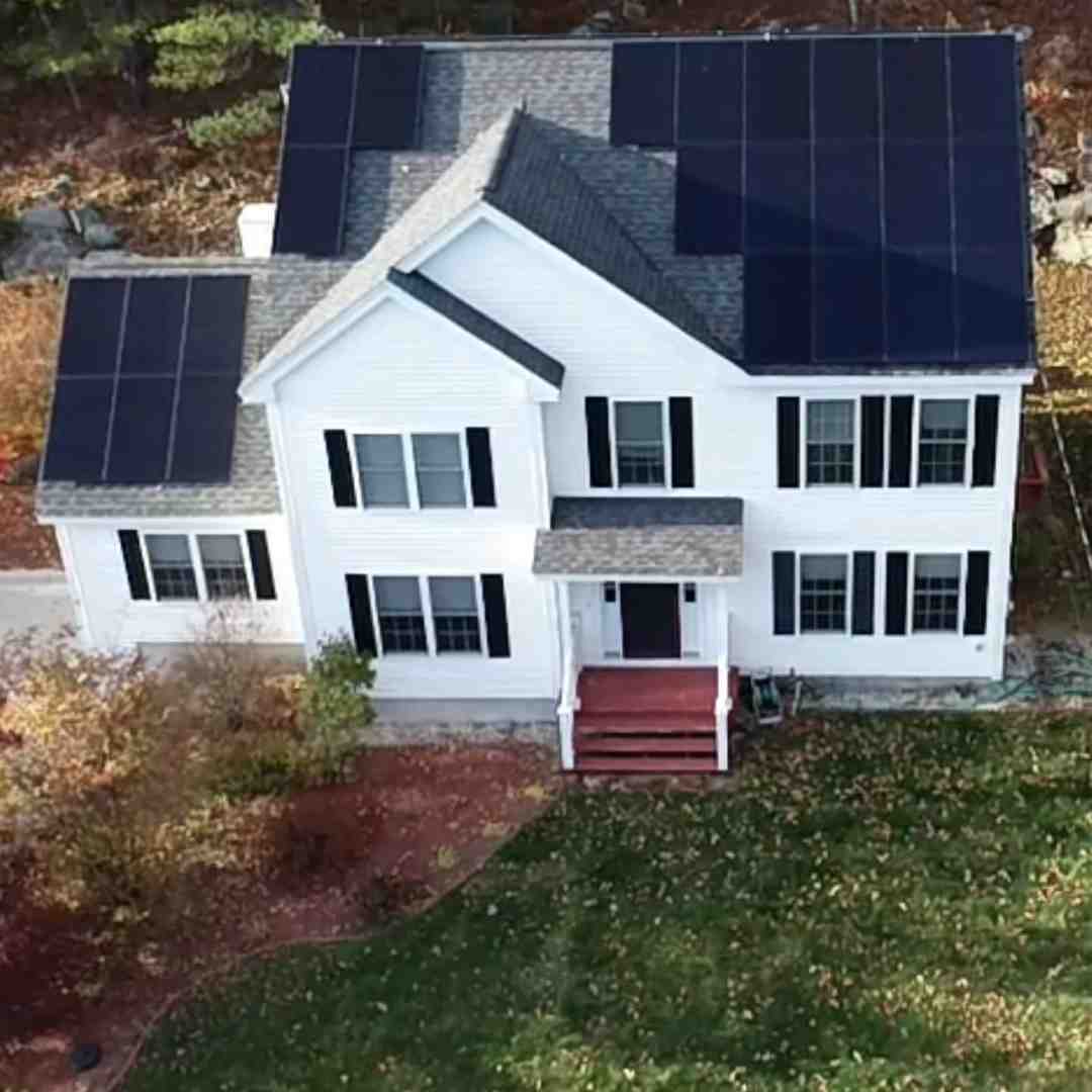 A two-story white house with black shutters and solar panels on the roof, surrounded by autumn foliage and a green lawn.