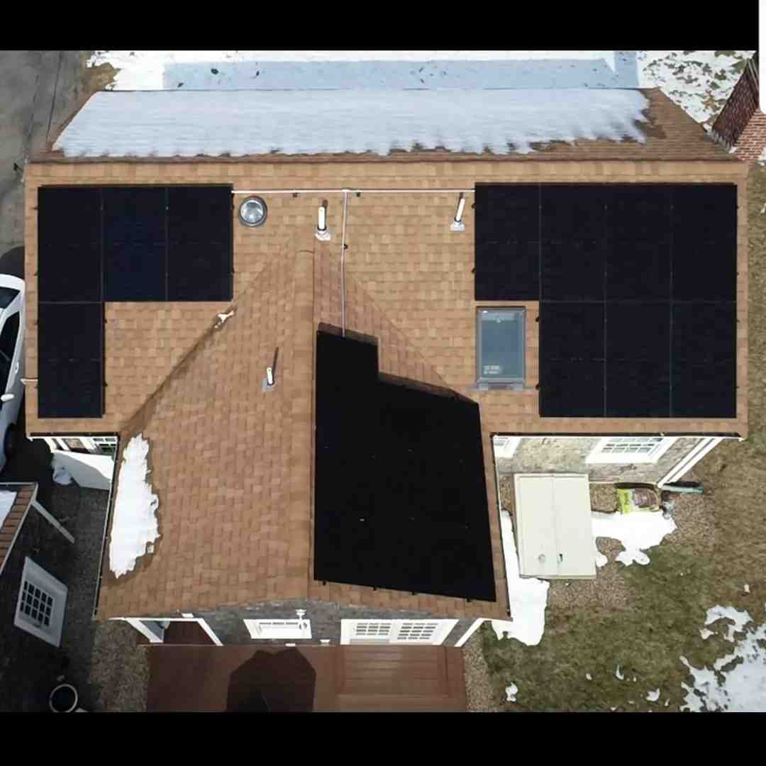 Aerial view of a house with solar panels on the roof, patches of snow, and some grass visible around the property.
