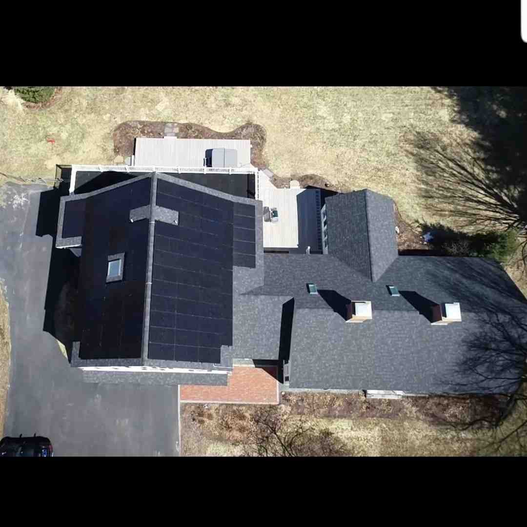 Aerial view of a house with black solar panels installed on the roof, surrounded by a yard and driveway.