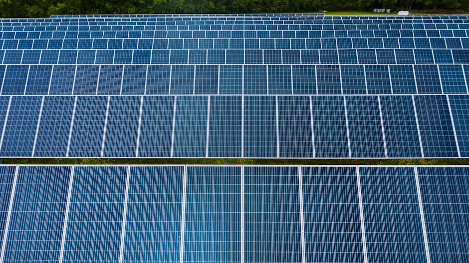 Aerial view of blue solar panels in a grid, surrounded by green vegetation—showcasing nh solar power incentives at work.