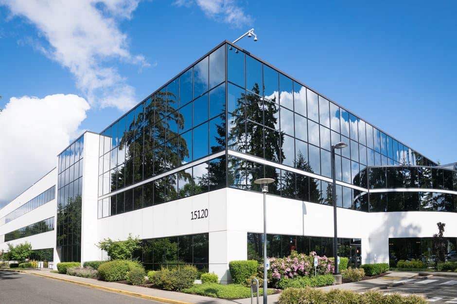 Modern glass office building at 15120 with mirrored windows reflecting trees and sky, featuring nh solar power incentives and surrounded by greenery.