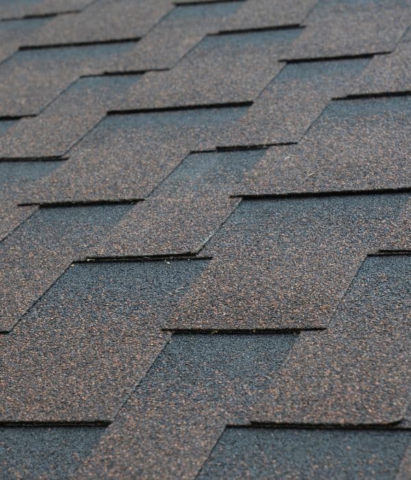 Close-up of overlapping asphalt roof shingles with a textured surface in brown and gray tones, highlighting quality and reliable roofing warranties.