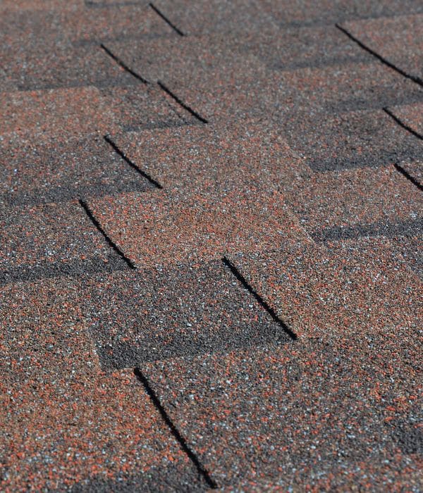 Close-up of asphalt roof shingles in brown, orange, and gray shades, arranged in an overlapping pattern. Ask about our Roofing Warranties.