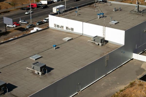 Flat rooftop of a commercial building with HVAC units and ladders, showcasing expert Commercial Roofing Services next to a busy road with cars.